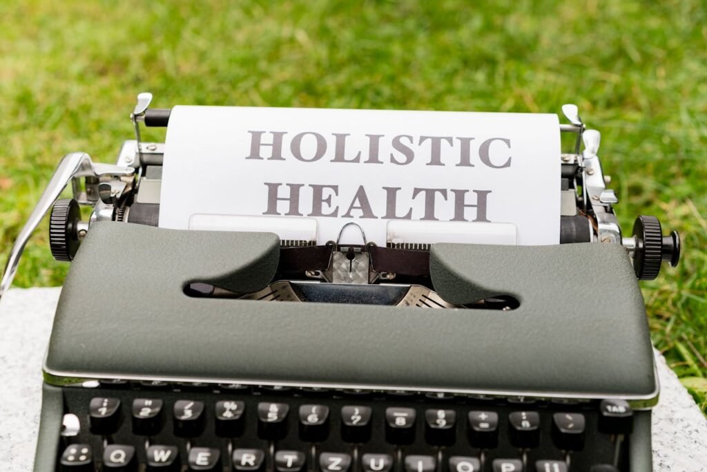 A vintage typewriter in a grassy outdoor setting displaying 'Holistic Health' on paper.